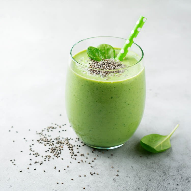 Green smoothie in a clear glass with a green polka-dot straw, topped with chia seeds and a spinach leaf garnish.