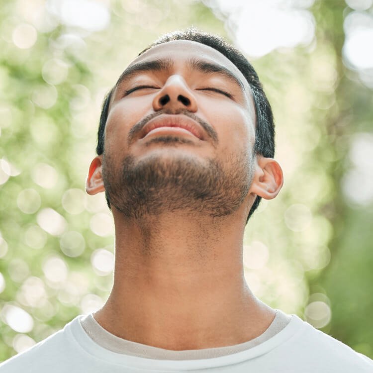 Man tilts his head up with eyes closed, outdoors, enjoying sunlight and fresh air.