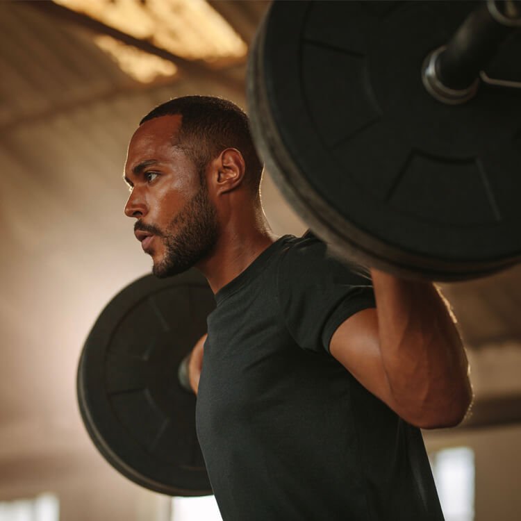 Man lifting a loaded barbell on his shoulders, performing an overhead press in a gym.