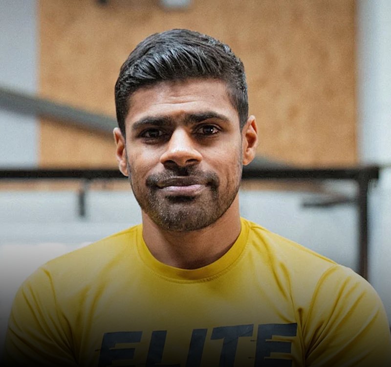 Portrait of a man with short black hair and a trimmed beard wearing a bright yellow Elite t-shirt, indoors.
