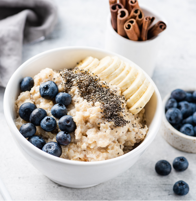 Bowl of oatmeal topped with blueberries, banana slices, and chia seeds in a white bowl with cinnamon sticks nearby.