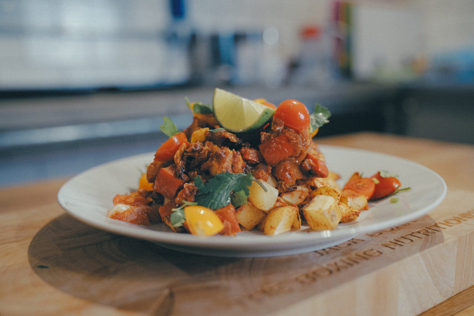 Plate of Mexican-inspired tacos with diced meat, peppers, herbs, and a lime wedge on top, served on a white plate