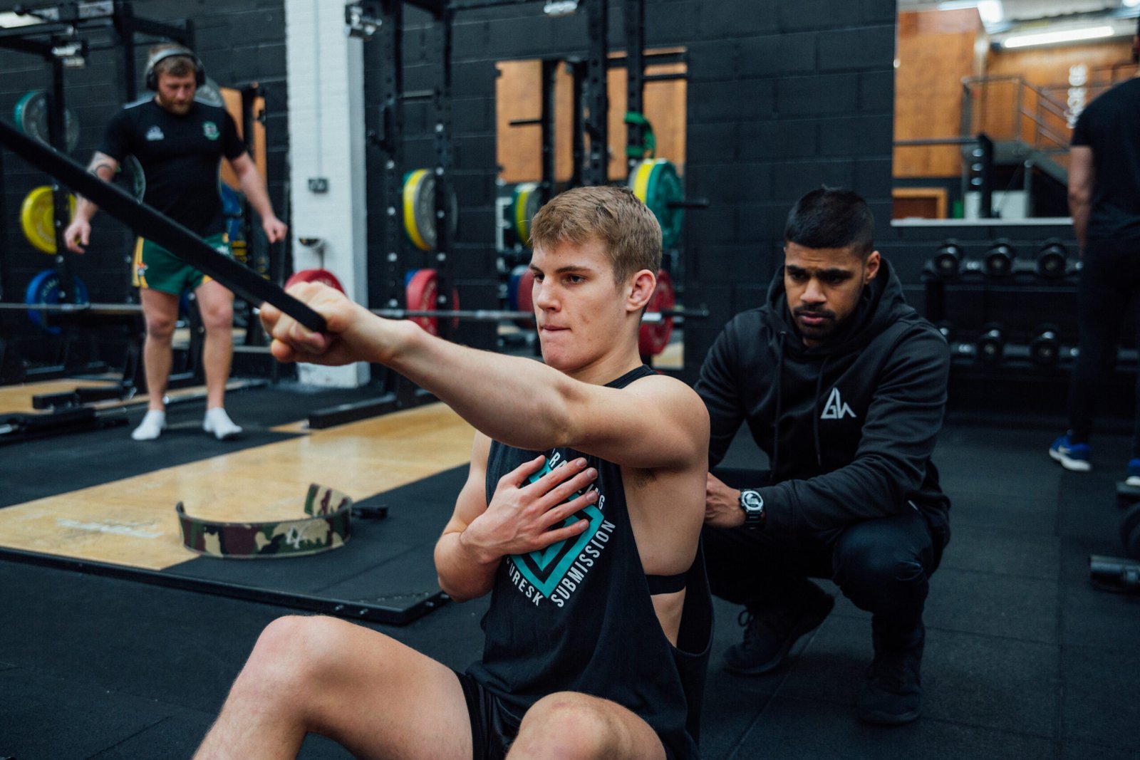 IMG_6891 Trainer assists a man performing a chest stretch with a resistance band in a gym.