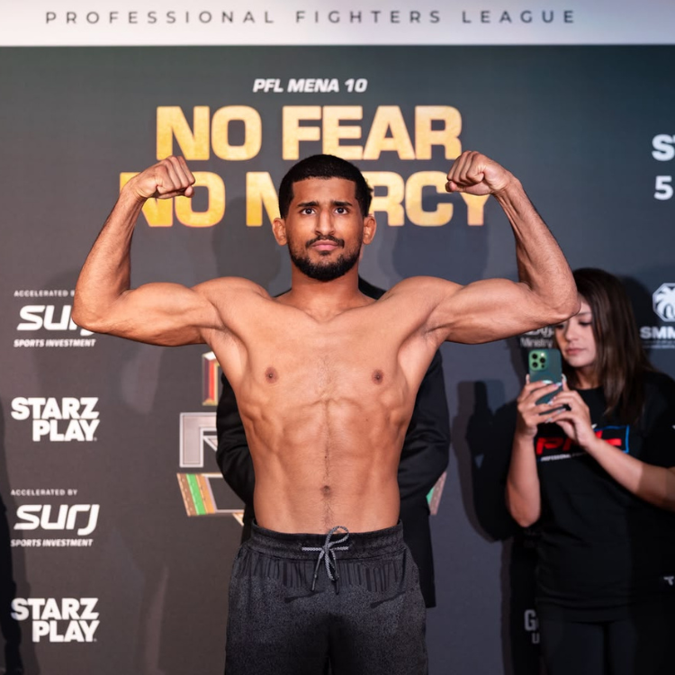Male professional fighter shirtless, flexing biceps on a stage with NO FEAR NO MERCY in the background.