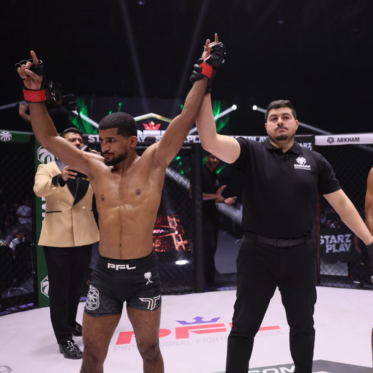 MMA fighter with arms raised in victory inside the cage, referee holding his wrist in a win gesture.